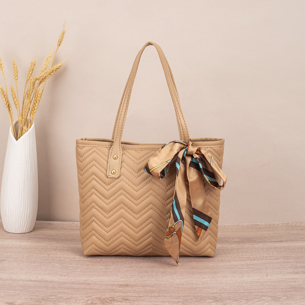 Beige quilted handbag with a matching scarf on a wooden surface and beige background