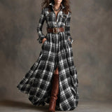 Woman wearing a long plaid dress with a belt and brown boots against a gray background