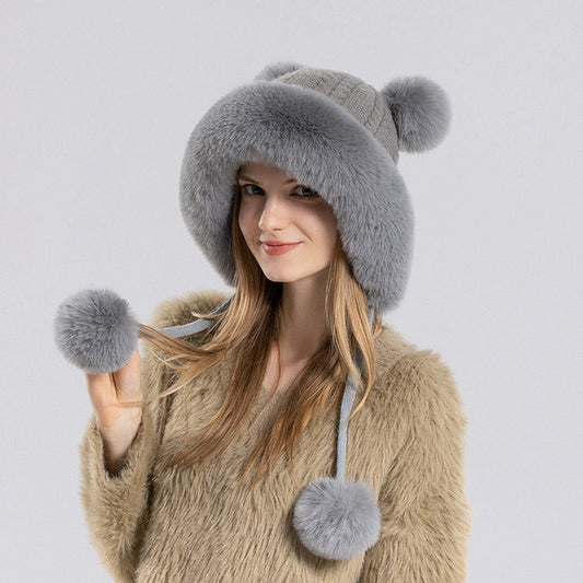 Woman wearing a gray fur hat with pom-poms on a light gray background