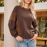 Woman wearing a brown sweater with patterned sleeves leaning against a column outdoors.