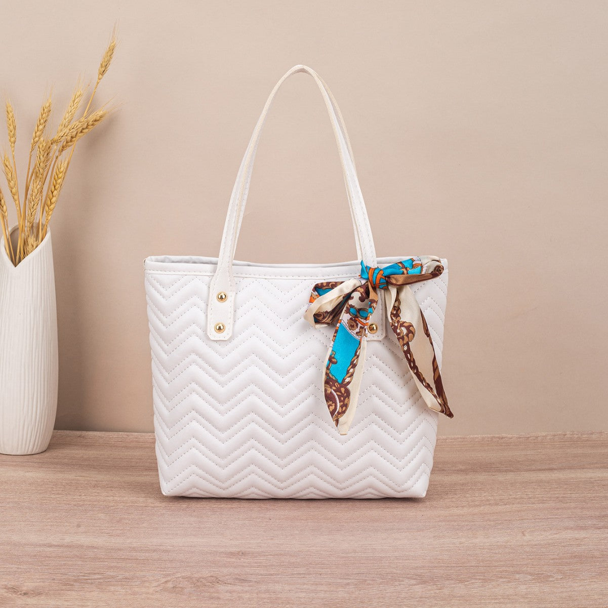 White quilted handbag with a decorative ribbon on a wooden surface and beige background