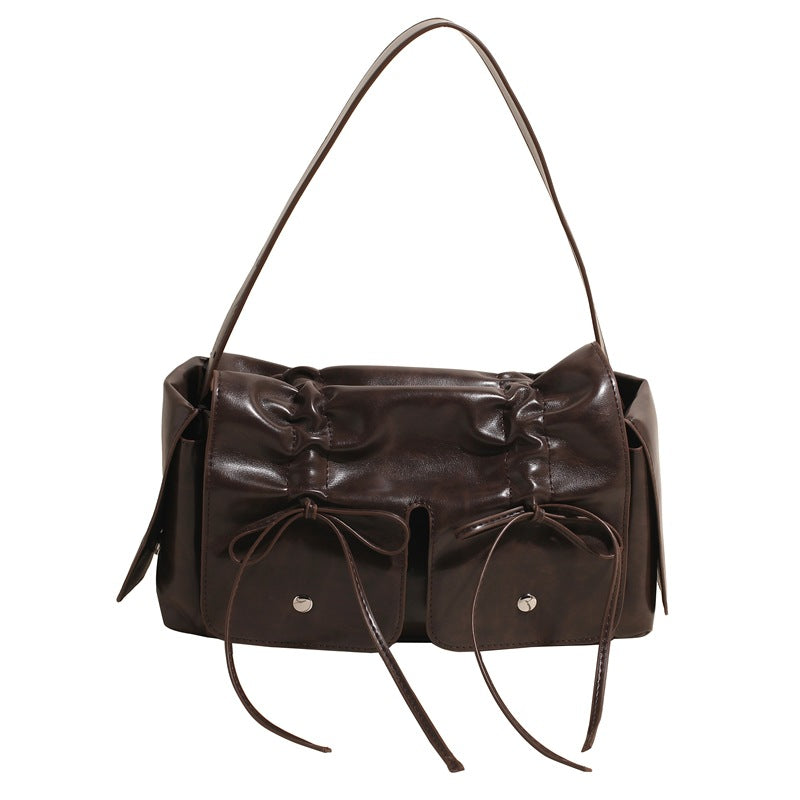 Brown leather handbag with decorative bows on a white background