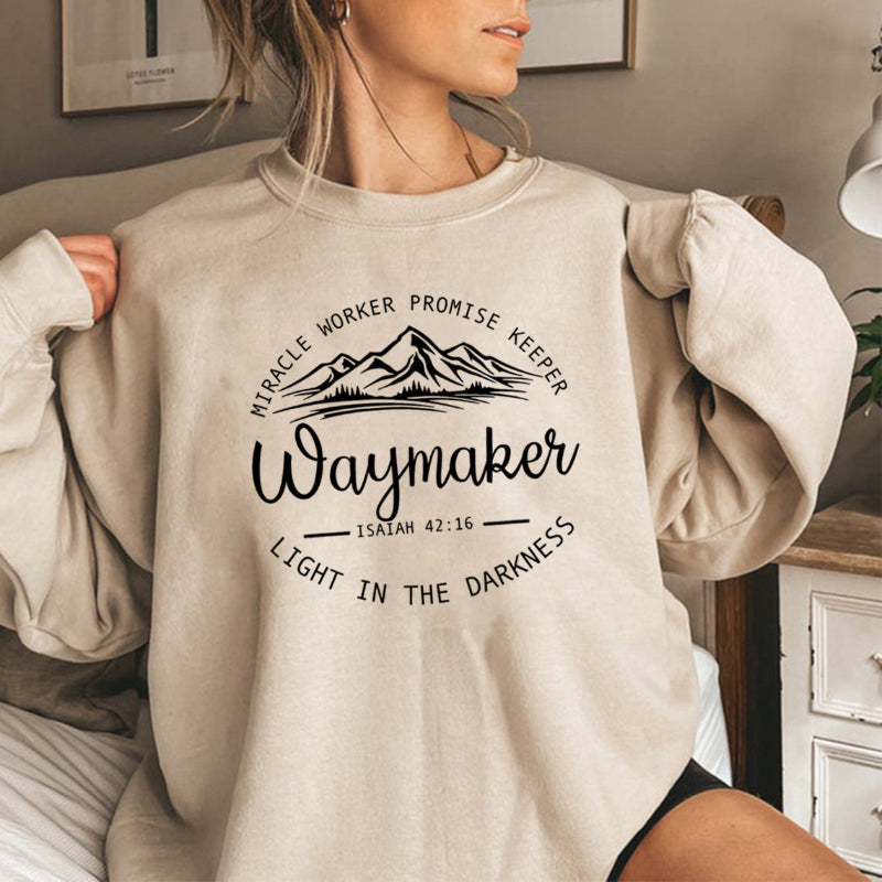 Person wearing a beige sweatshirt with motivational text and mountain graphic