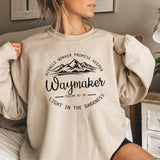 Person wearing a beige sweatshirt with motivational text and mountain graphic