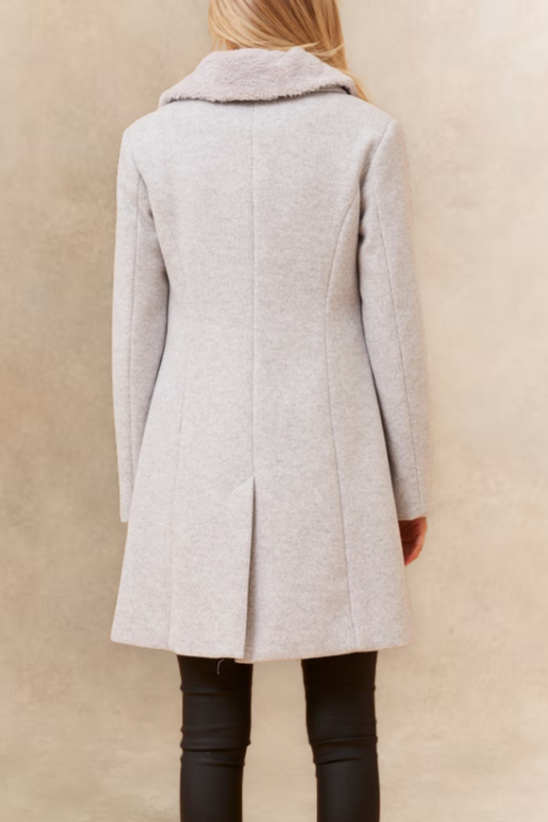 Person wearing a light gray coat against a beige background