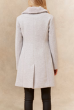 Person wearing a light gray coat against a beige background