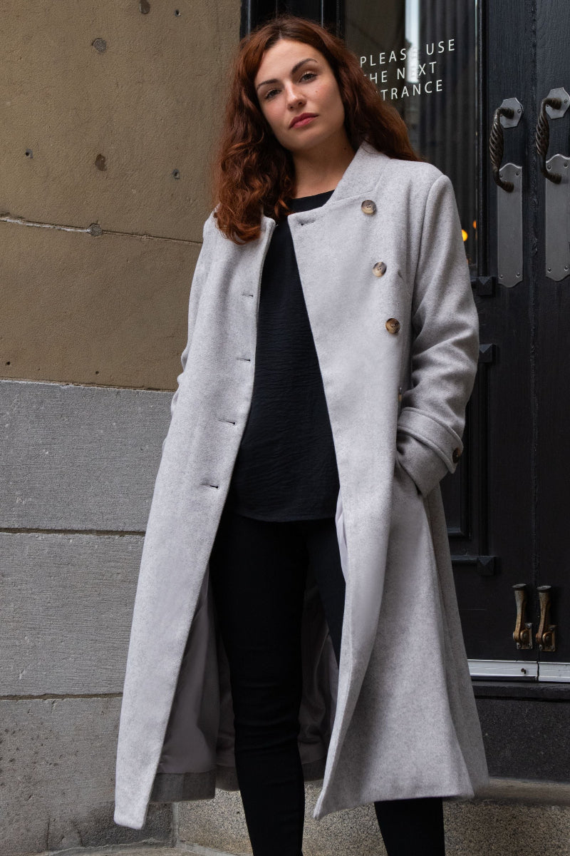Woman wearing a gray coat standing outside a building.