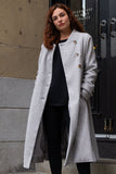 Woman wearing a gray coat standing outside a building.