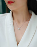Necklace with a small round pendant worn by a person in a white blazer.