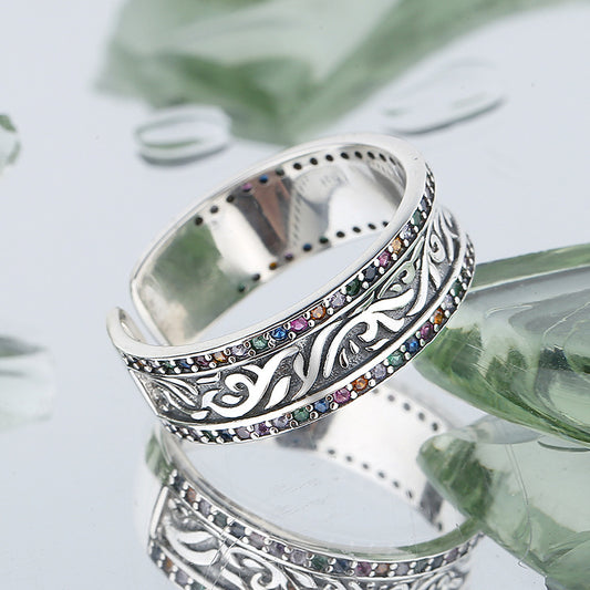Silver ring with colorful stones on a reflective surface with green leaves in the background