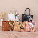 Five handbags in different colors with decorative ribbons on a wooden surface.