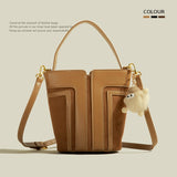 Brown leather handbag with a small plush toy attached to the strap on a beige background