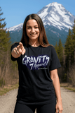 Woman wearing a black t-shirt with 'Gravity Apparel' logo in a mountainous landscape