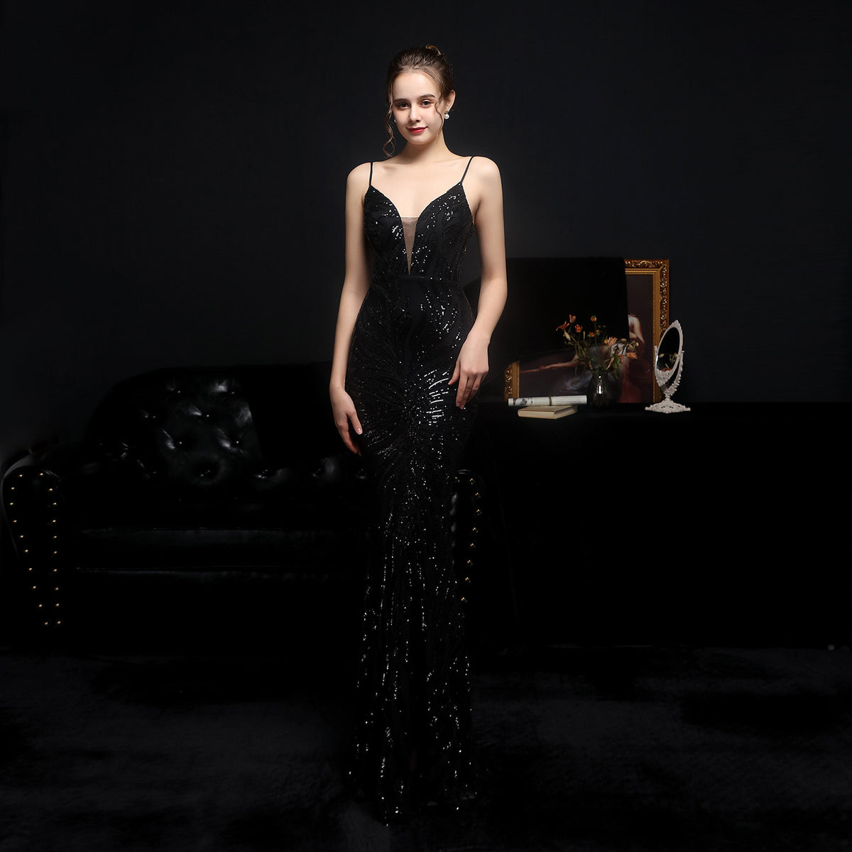 Woman in a black sequin dress standing in a dimly lit room with a dark background.