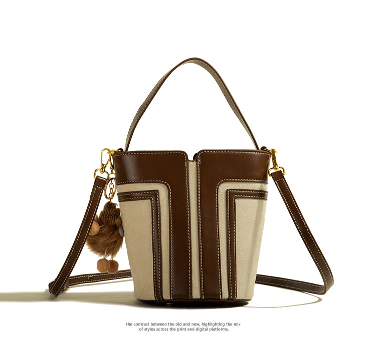 Brown and beige handbag with a decorative charm on a white background