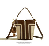 Brown and beige handbag with a decorative charm on a white background
