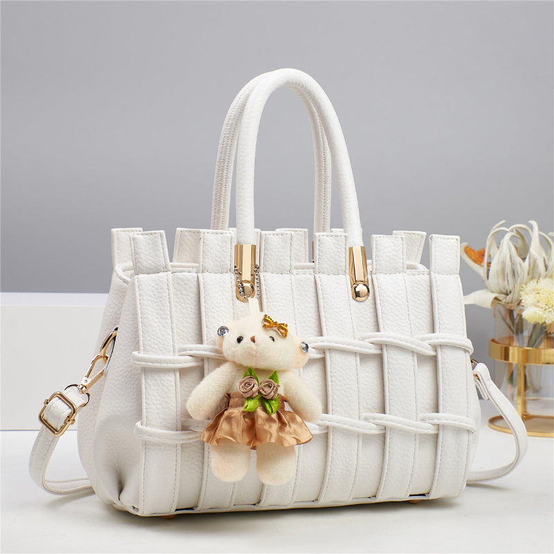 White woven handbag with a teddy bear keychain on a light gray background