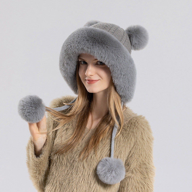 Woman wearing a gray fur hat with pom-poms on a light gray background