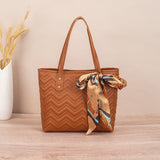 Brown quilted handbag with a colorful scarf on a wooden surface and beige wall background