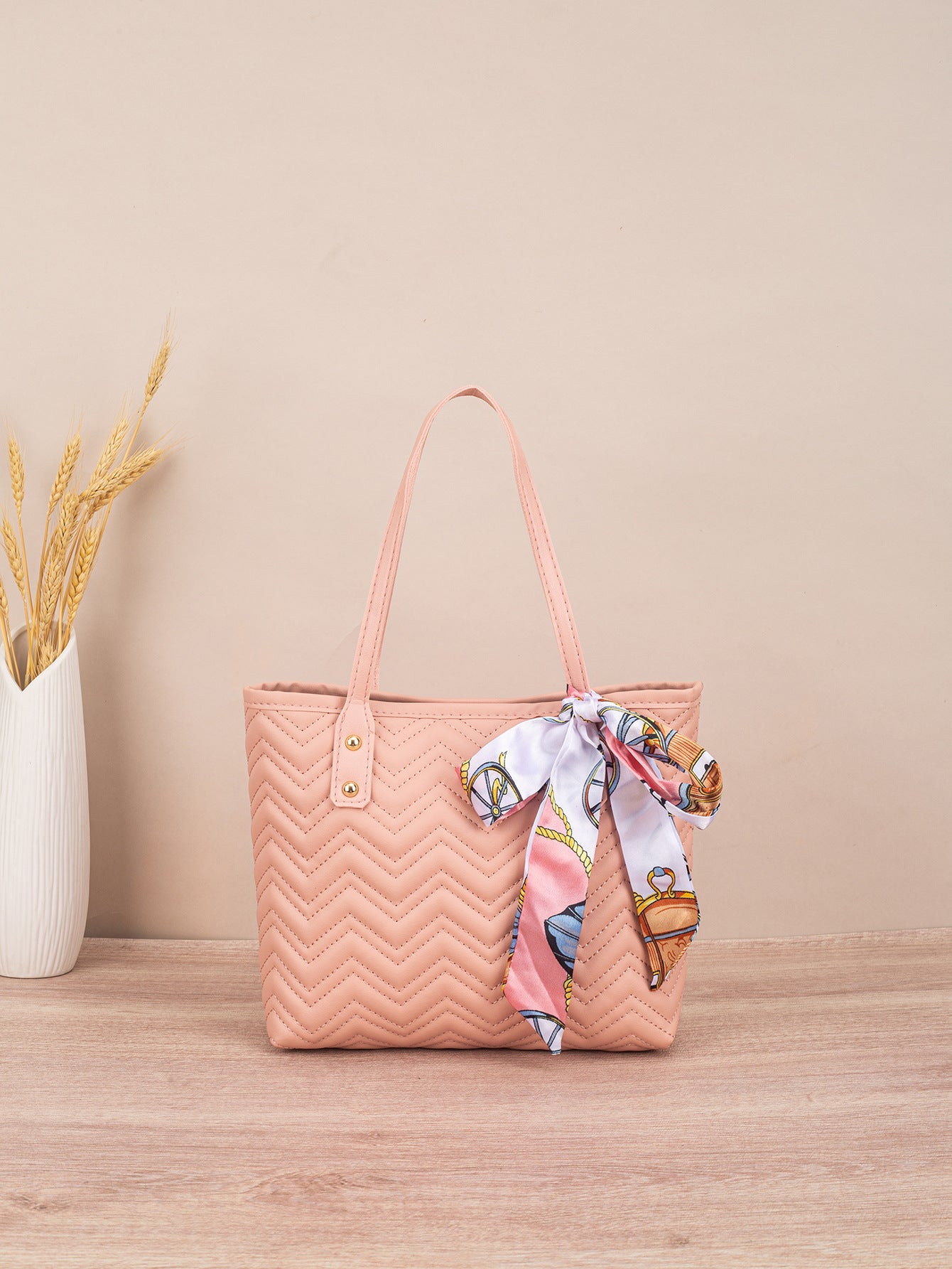 Pink quilted handbag with a colorful scarf on a wooden surface and beige wall background
