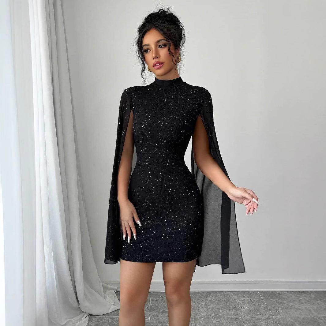 Woman wearing a black dress with cape sleeves against a gray curtain background