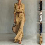 Woman wearing a long beige dress with a belt, holding a bag, against a neutral background.