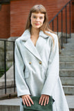 Woman wearing a light gray coat standing outdoors on steps.
