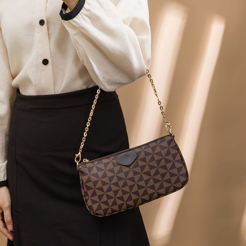 Person holding a patterned handbag with a gold chain strap against a neutral background