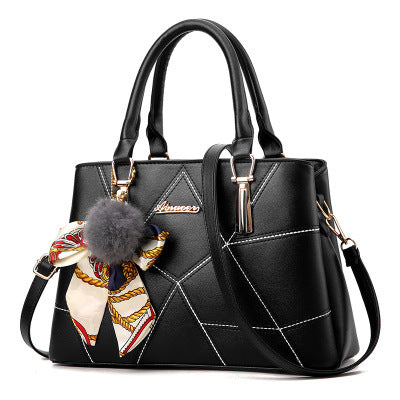 Black handbag with decorative scarf and pom-pom on a white background