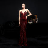 Woman in a red evening gown standing in a dark room with a black sofa and framed picture in the background.