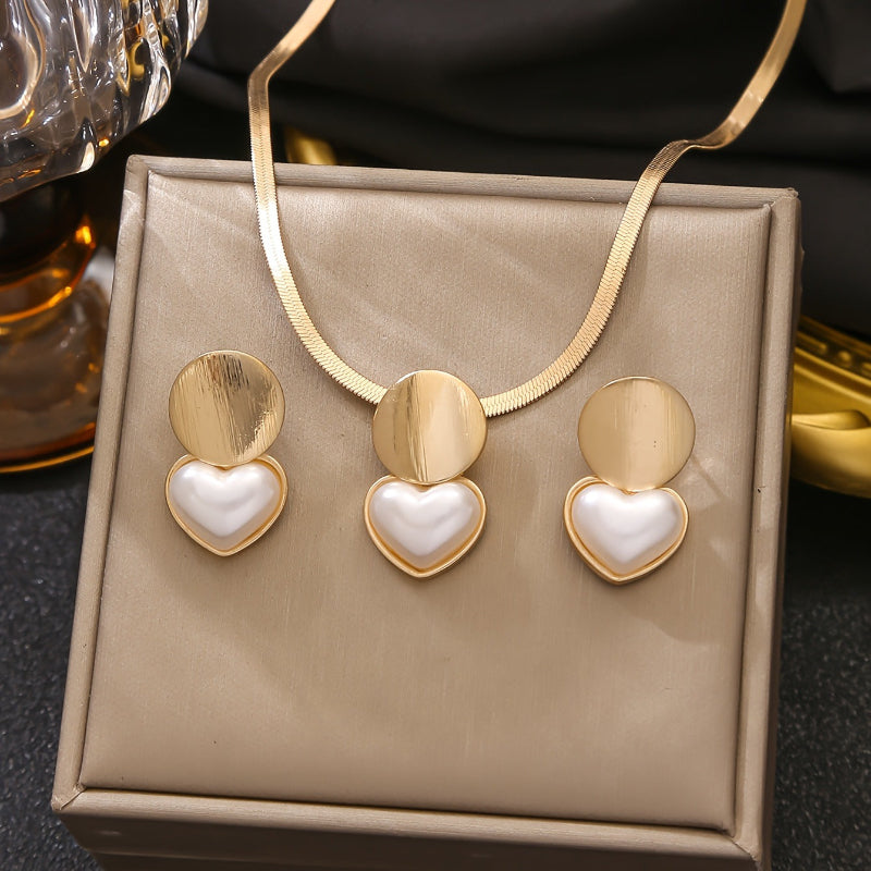 Gold and white heart-shaped earrings on a beige jewelry box with a gold necklace.