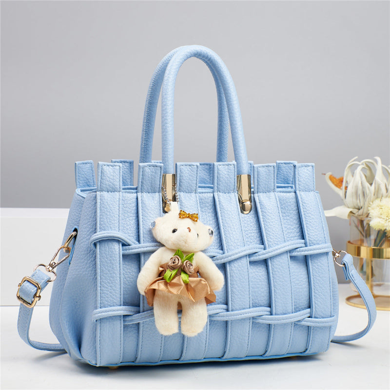 Light blue handbag with a teddy bear keychain on a gray background
