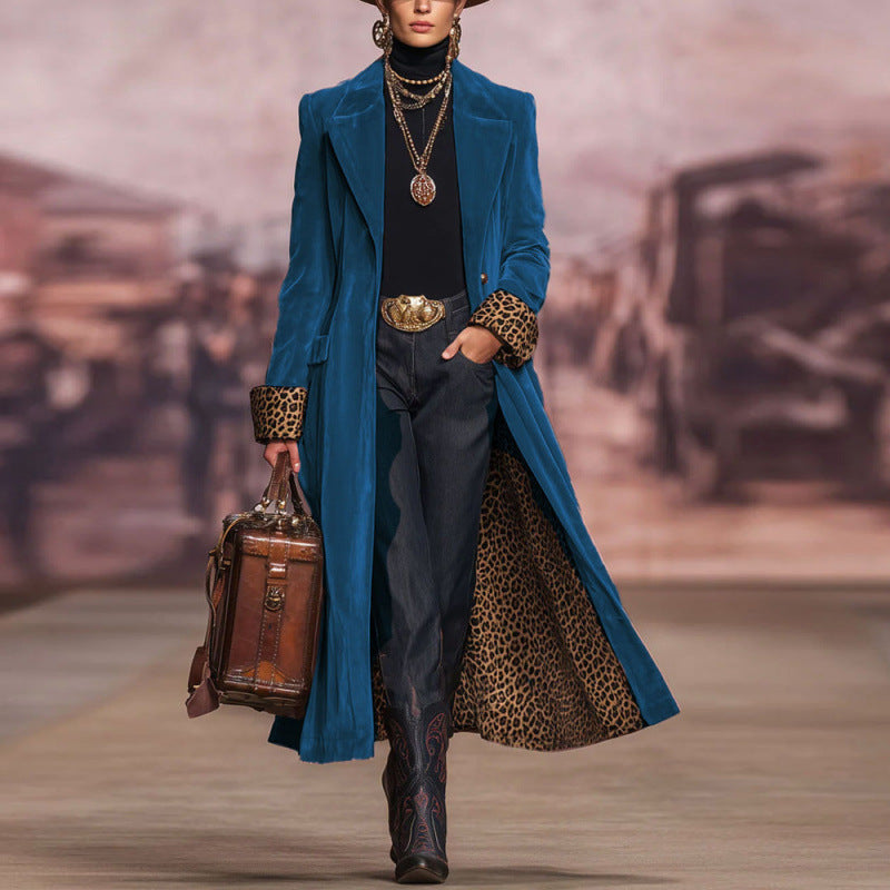 Model wearing a blue coat with leopard print accents, holding a suitcase on a runway.