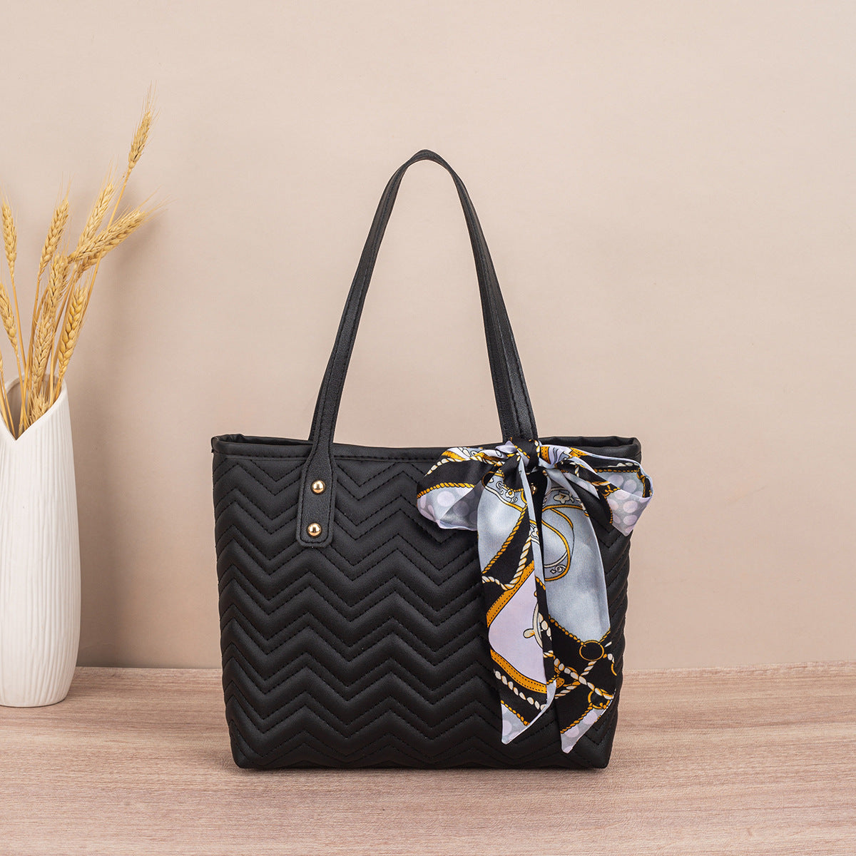 Black quilted handbag with a patterned scarf tied around it on a wooden surface.