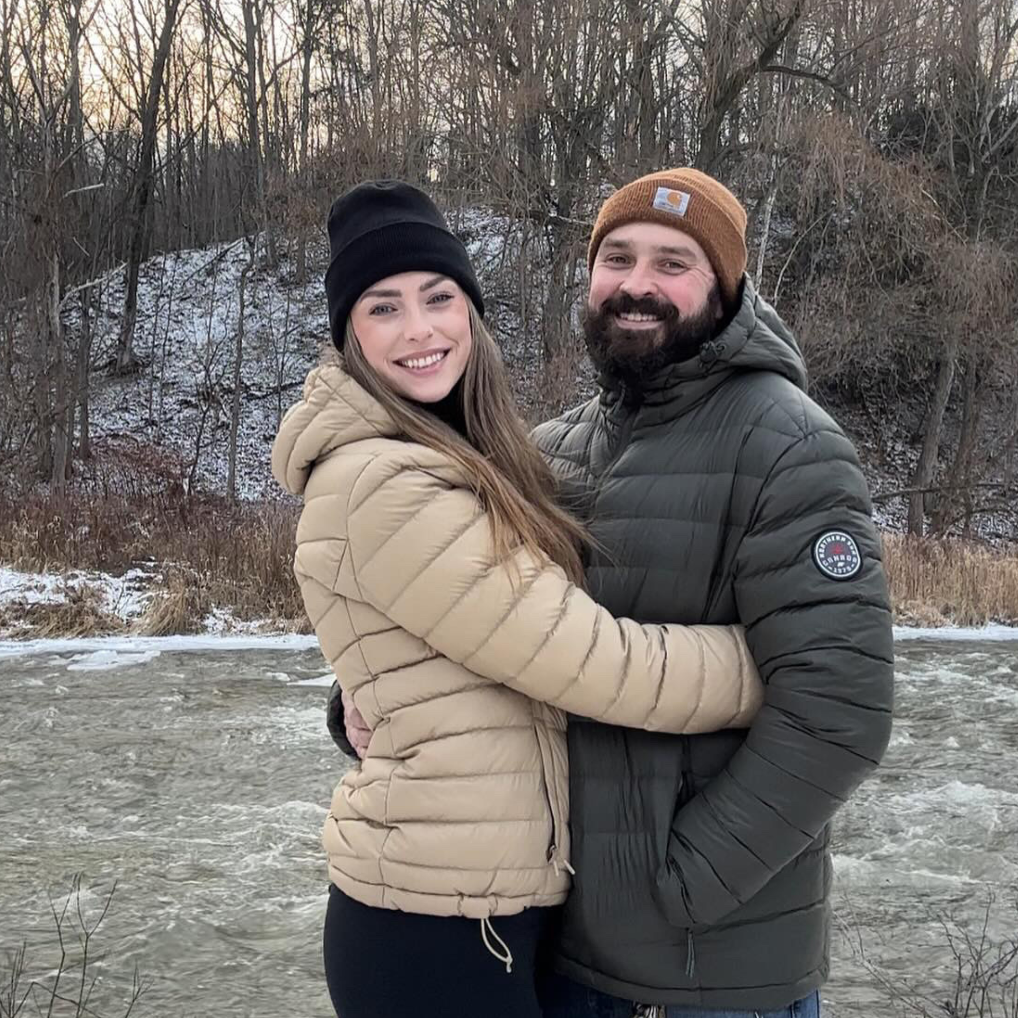 Two people hugging outdoors in a snowy landscape with trees.